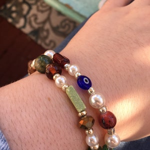 May include: Two bracelets with colorful beads, including white pearls, green, brown, and blue glass beads, and a blue evil eye charm.