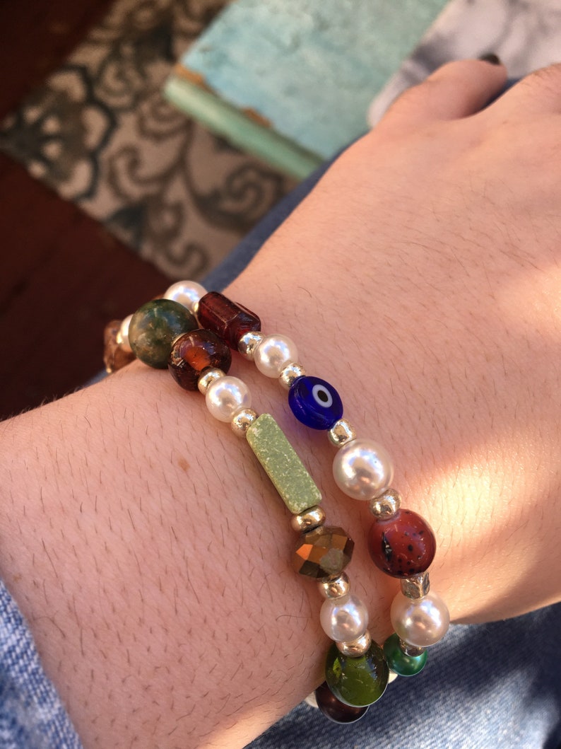 May include: Two bracelets with colorful beads, including white pearls, green, brown, and blue glass beads, and a blue evil eye charm.