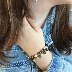 May include: A woman wearing a denim jacket with a mushroom-shaped earring and two beaded bracelets on her wrist. The bracelets are made of green, brown, and white beads.