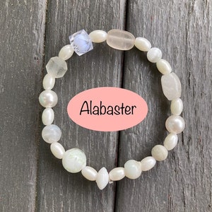 May include: A white bracelet made of alabaster beads, pearls, and glass beads. The bracelet features a light blue glass bead with a white swirl design.