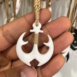 May include: A white bone anchor pendant with intricate carvings hangs from a brown rope necklace.