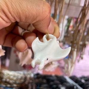 Op de afbeelding: Witte gegraveerde rog-hanger aan een bruin koordsnoer. De hanger is gedetailleerd met een getextureerd oppervlak en een klein oog.