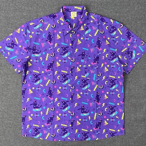 May include: Purple button-down shirt with a repeating pattern of black cats skateboarding, along with geometric shapes and lightning bolts in pink, yellow, and blue. The shirt has short sleeves and a collared neckline.