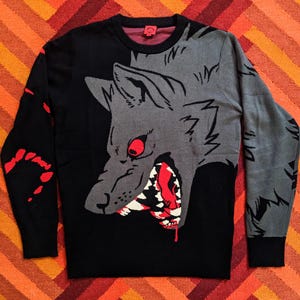 May include: Black sweater with a grey wolf graphic. The wolf has red eyes and a bloody mouth. The sweater has red blood splatter details.