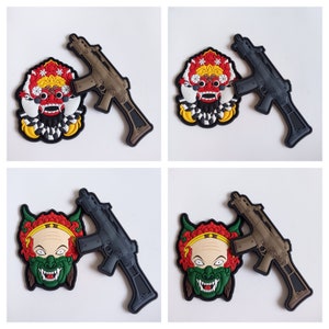 Może przedstawiać: Cztery haftowane łatki przedstawiające stylizowaną maskę demona w kolorze czerwonym, białym i czarnym. Każda łatka jest połączona z czarną i brązową zabawkową bronią.