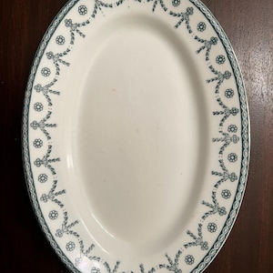 May include: White oval serving platter with a green floral border. The border features a repeating pattern of small flowers and bows.