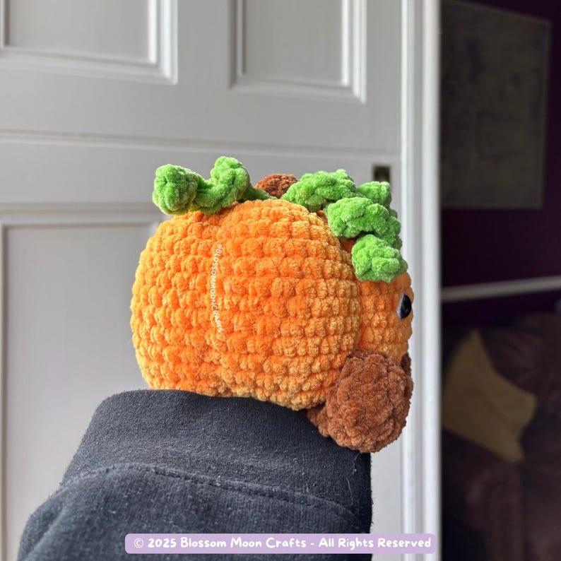 May include: A crocheted pumpkin in shades of orange, brown, and green. The pumpkin has a textured surface and is topped with green leaves and a brown stem. The pumpkin is a handmade item, perfect for fall decor.