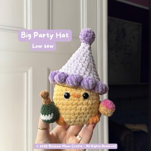 May include: A crocheted yellow chick wearing a white and purple party hat, holding a green bottle and a pink donut. The text "Big Party Hat" and "Low sew" are visible on the image. The chick has black eyes and orange feet.