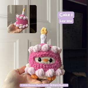 May include: A handmade crochet cake in pink, white, and yellow. The cake has a candle on top and is decorated with white frosting. The text "Cake 1 Low sew" is visible. The copyright text "&copy; 2026 Blossom Moon Crafts - All Rights Reserved" is also visible.