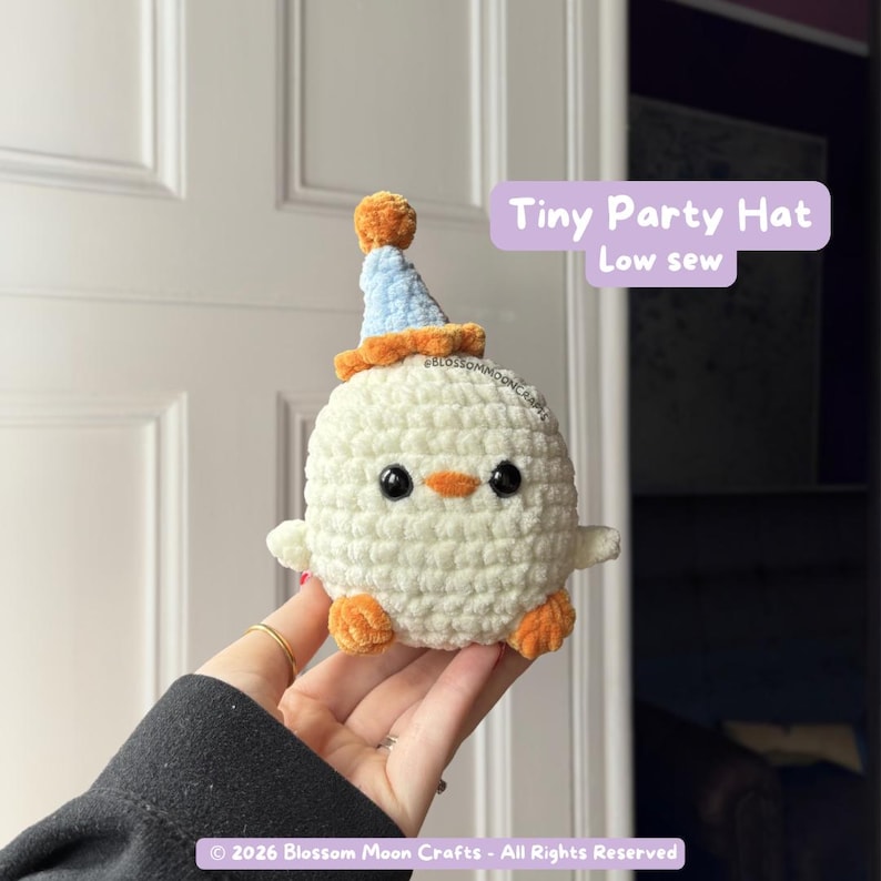 May include: A crocheted chick with a party hat. The chick is white with orange feet and beak, and black eyes. The party hat is blue with an orange brim and top. Text on the image reads "Tiny Party Hat Low sew".