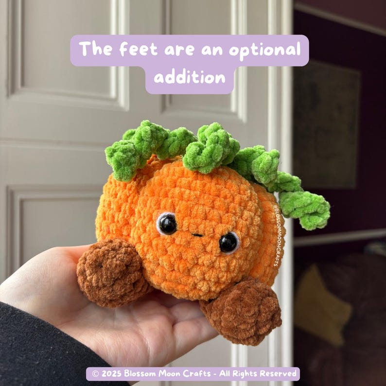 May include: An orange crocheted pumpkin plushie with green vine-like leaves and brown feet. The pumpkin has black eyes and a small smile. Text on the image reads "The feet are an optional addition."