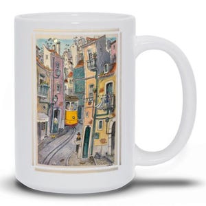 May include: A white ceramic mug with a colorful illustration of a yellow tram traveling through a narrow street lined with buildings. The buildings are painted in shades of yellow, pink, and blue, with windows and balconies. The mug has a white handle.