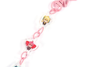 Puede incluir: Un llavero rosa con tres colgantes de personajes de estilo anime. Los colgantes son transparentes con ilustraciones coloridas de personajes. El llavero tiene un cierre en forma de estrella y una cadena de eslabones rosas.