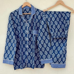 K&ouml;nnte beinhalten: Ein blaues und wei&szlig; gemustertes Pyjama-Set mit einem lang&auml;rmeligen Oberteil und einer Hose. Das Set h&auml;ngt an zwei Holzb&uuml;geln.