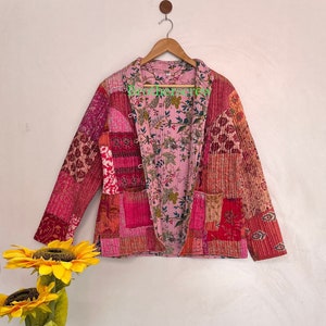 Könnte beinhalten: Eine rosafarbene und rote Patchwork-Steppjacke mit einem floralen Futter. Die Jacke hat einen Knopfverschluss und lange Ärmel.