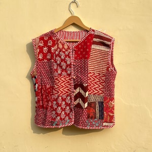 May include: A red quilted vest with a patchwork design. The vest has a button closure and is sleeveless.