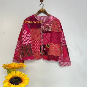 Peut inclure: Une veste matelassée rose avec un motif patchwork. La veste a une fermeture éclair et des manches longues. Le tissu est un mélange de différents motifs et couleurs, dont le rose, le blanc et le noir.