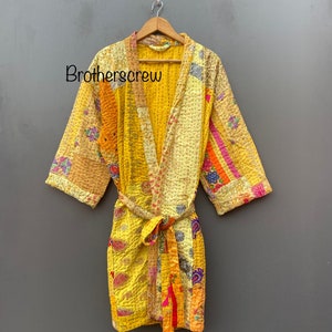 Può includere: Una vestaglia gialla trapuntata con un motivo a patchwork colorato. La vestaglia ha una cintura da legare e maniche lunghe.