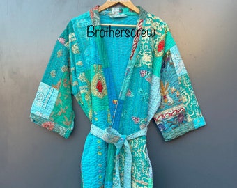 Op de afbeelding: Een turquoise blauwe gewatteerde badjas met een patchwork ontwerp en bloemenborduurwerk. De badjas heeft een strikceintuur en hangt aan een houten hanger. De tekst "Brothercrew" is zichtbaar op de badjas.