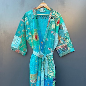 May include: A turquoise blue quilted robe with a patchwork design and floral embroidery. The robe has a tie belt and is hanging on a wooden hanger. The text "Brothercrew" is visible on the robe.