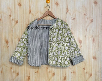 May include: A green and white floral patterned jacket with black and white striped sleeves. The jacket is hanging on a wooden hanger against a woodgrain background.