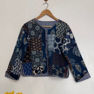Könnte beinhalten: Eine blaue gesteppte Jacke mit Patchwork-Design, das verschiedene florale und geometrische Muster zeigt. Die Jacke hat einen runden Ausschnitt und lange Ärmel.