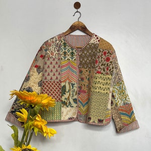 Pode incluir: Uma jaqueta acolchoada de patchwork com uma variedade de padrões florais e geométricos em tons de marrom, rosa, verde e azul. A jaqueta tem um decote redondo e mangas compridas.