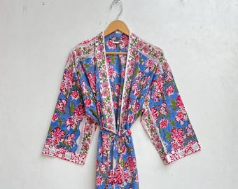 May include: A blue floral print robe with a white trim and a matching tie. The robe features a vibrant pattern of pink flowers and green leaves. The robe is hanging on a wooden hanger.