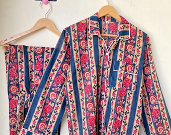 Può includere: Un completo pigiama a due pezzi con motivo floreale. Il set comprende una camicia a maniche lunghe con bottoni e pantaloni abbinati. Il design presenta strisce verticali blu navy, beige e rosa, con finiture bianche.