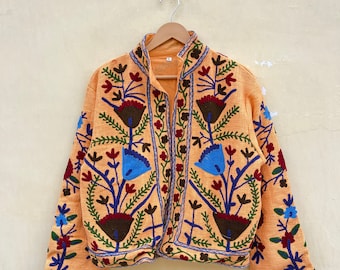 May include: A light orange embroidered jacket with a floral pattern in shades of blue, red, green, and brown. The jacket has a mandarin collar and a button closure.
