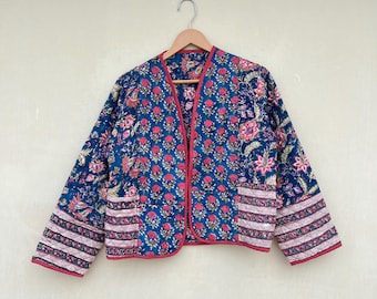 Op de afbeelding: Een blauw gewatteerd jack met een bloemenprint en rode bies. Het jack heeft een knoopsluiting en twee zakken.