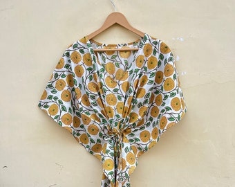 May include: A white cotton kaftan with a yellow and green floral print. The kaftan has a V-neck and short sleeves. It is tied at the waist with a sash.