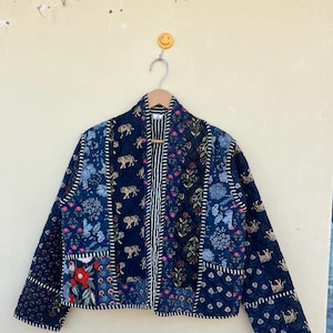 May include: A blue quilted jacket with a floral and animal print. The jacket has a striped trim and a front zip closure.