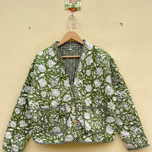 Peut inclure: Une veste matelassée verte avec un imprimé floral blanc et une doublure rayée. La veste a une fermeture boutonnée et deux poches.