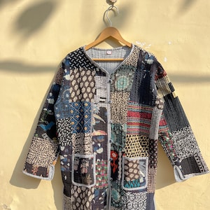 Puede incluir: Una chaqueta acolchada negra con un diseño de patchwork que presenta varios colores y patrones. La chaqueta tiene un cierre de botón y dos bolsillos.