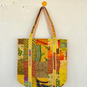 May include: A patchwork tote bag with yellow, orange, brown, and green fabric squares. The bag has white and yellow striped straps.