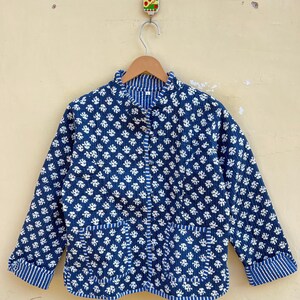 Peut inclure: Une veste matelassée bleue avec un imprimé floral blanc et un col mandarin. La veste a deux poches et une fermeture à boutons.