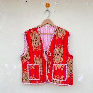 Puede incluir: Un chaleco rojo y blanco a rayas sin mangas con estampado de tigre. El chaleco tiene cierre de corbata y dos bolsillos.