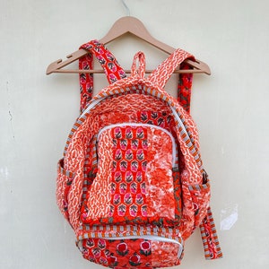 May include: A red and orange patchwork backpack with a floral print. The backpack has a zippered closure and adjustable straps.