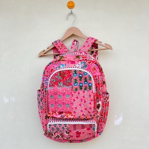 May include: A pink patchwork backpack with floral patterns and white stitching. The backpack is hanging on a wooden hanger.