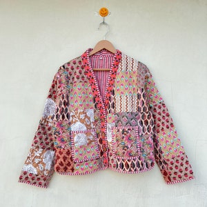 May include: A patchwork quilted jacket with a pink, brown, and white floral pattern. The jacket has a V-neck and a button closure.
