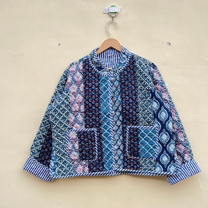 May include: A blue and white quilted jacket with a patchwork design. The jacket has a mandarin collar and a button closure. The sleeves have a striped cuff.