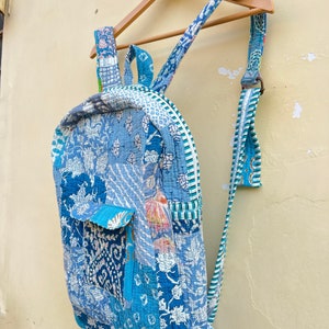 May include: A blue and white patchwork backpack with a zipper closure and a small pocket on the front. The backpack is made of quilted fabric and has a long strap.