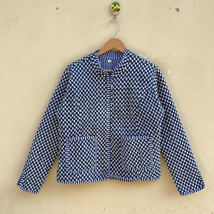 Puede incluir: Una chaqueta azul y blanca con estampado, cierre de cremallera y dos bolsillos. La chaqueta está colgada en una percha de madera.