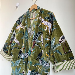 May include: Olive green velvet robe with a jungle animal print featuring zebras, leopards, toucans, and flamingos. The robe has white trim and striped cuffs. It is hanging on a wooden hanger.