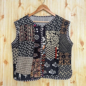 May include: A black quilted waistcoat with a patchwork design featuring various geometric and floral patterns in shades of brown, white, and black. The waistcoat has a button closure and a round neckline.