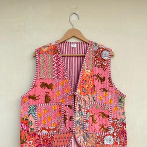 May include: A pink quilted vest with a patchwork design featuring various floral and animal prints. The vest has a V-neck and ties at the front.