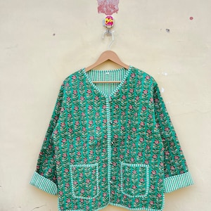 May include: A green quilted jacket with a floral print and a button closure. The jacket has two pockets and a striped lining.