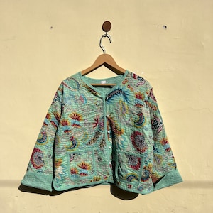 May include: A mint green quilted jacket with a floral print and button closure. The jacket has a relaxed fit and long sleeves.