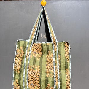 May include: A green and white striped tote bag with a tiger print. The bag has a light blue trim and two handles.